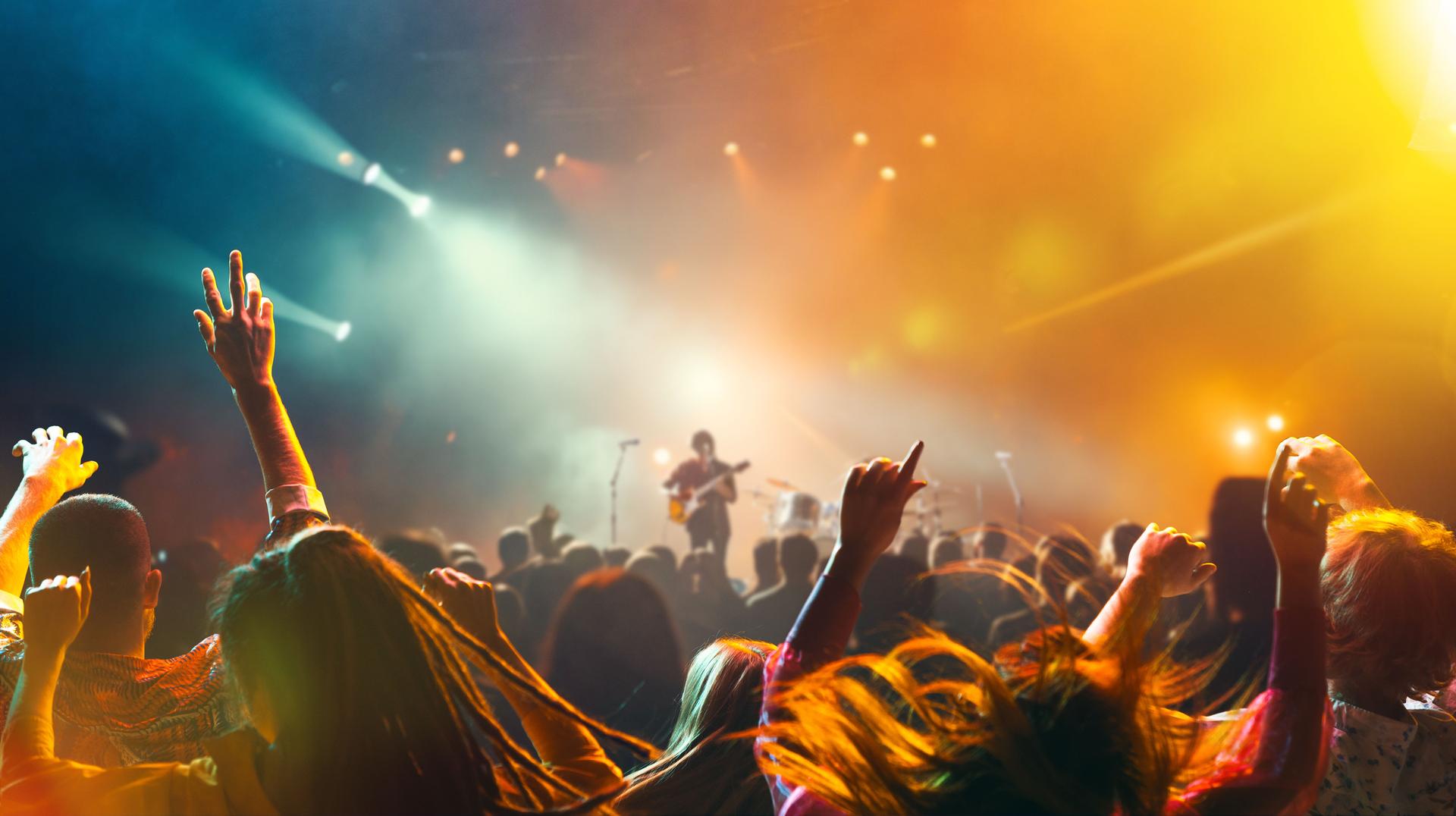 Crowded concert hall with stage, spotlight indoor and people silhouette dancing and singing on dancefloor during summer music festival.